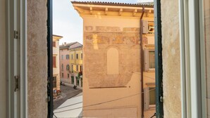 Une vue à travers la fenêtre d’un bâtiment, donnant sur une scène de rue, avec notamment un immeuble orné d’une fresque murale, une rue où sont garées des voitures et une personne.