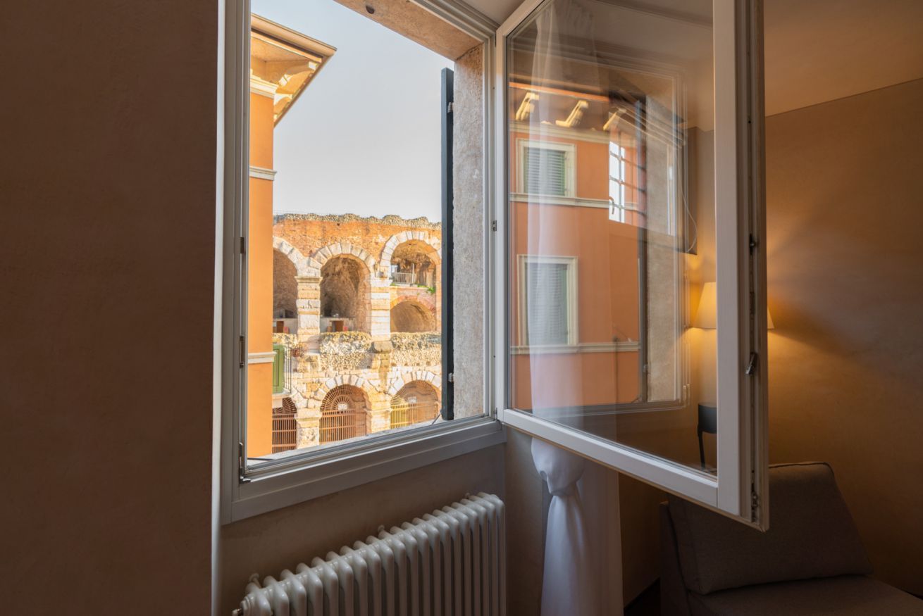 Ein Zimmer mit Fensterblick auf eine alte Steinarchitektur, einem Heizkörper und einem Sessel.