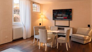 Un salon moderne avec une table à manger en verre, quatre chaises, un canapé, un téléviseur fixé au mur, une fenêtre avec des rideaux et un radiateur.
