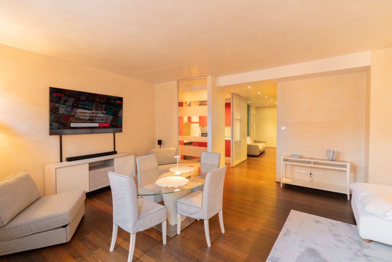 Una sala de estar moderna con un televisor de pantalla plana, una mesa de comedor con sillas, un sofá y una consola blanca.