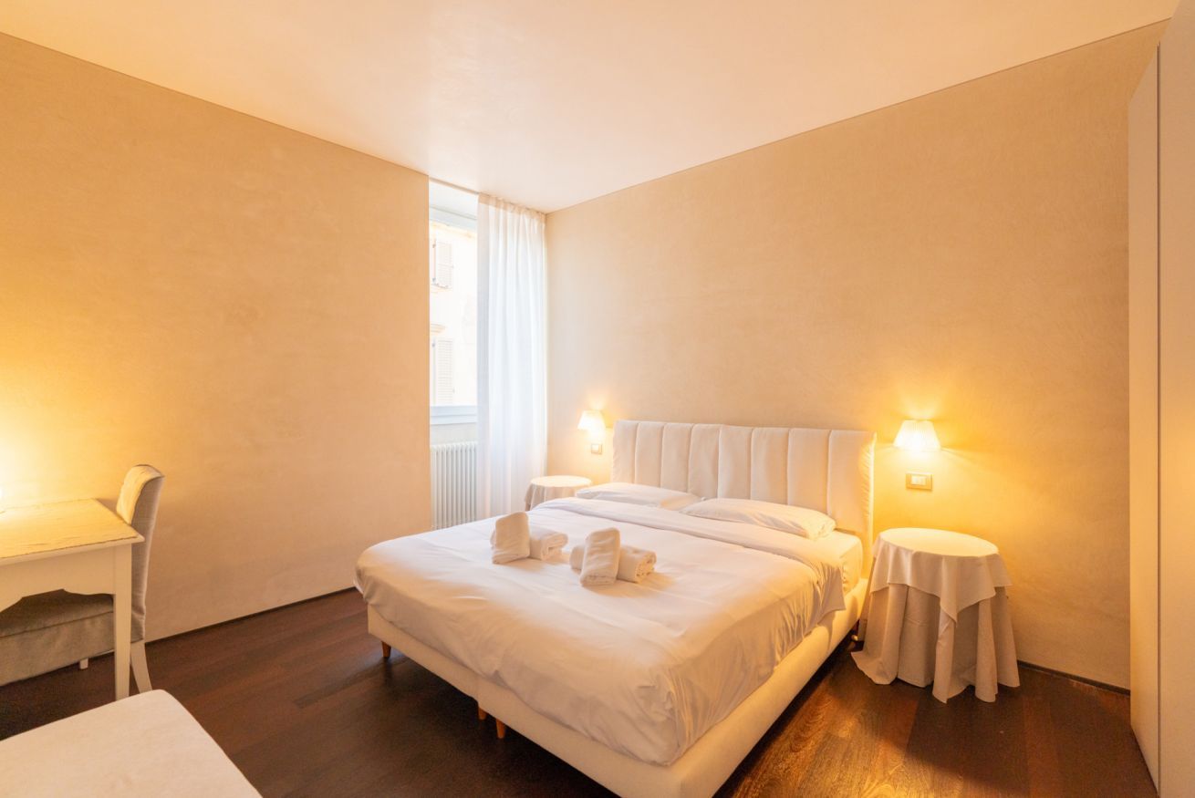 Une chambre d’hôtel avec un grand lit, deux tables de chevet, une chaise et une fenêtre avec des rideaux.