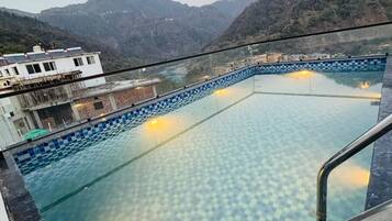 A swimming pool with a checkered pattern, surrounded by a building with a balcony overlooking a mountainous landscape.