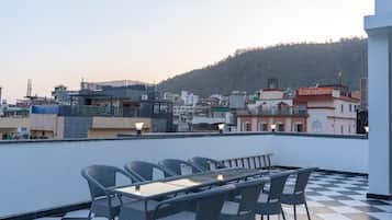 Una terraza en la azotea con suelo a cuadros, mobiliario de mimbre y vistas a un paisaje urbano con edificios y una colina.