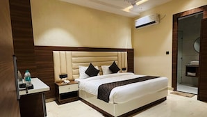 A modern hotel room with a large bed, bedside tables, a desk, and a bathroom visible through a glass door. - Hotel Hrishikesh High Tapovan 2.0 (Rishikesh)