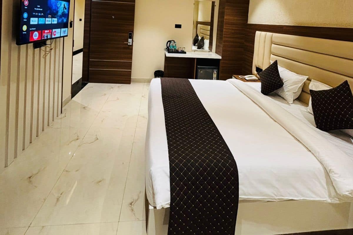 A hotel room with a bed, a TV mounted on the wall, a ceiling fan, and a minibar.