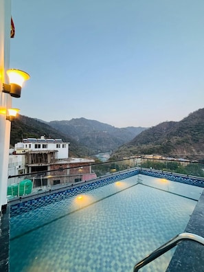 Una piscina con un diseño de mosaicos, rodeada por una barandilla, con vista a un paisaje montañoso de fondo.