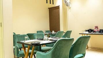 A dining area with a table set for six, green upholstered chairs, and pendant lighting.