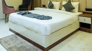 Una habitación de hotel moderna con una cama grande, mesitas de noche, un ventilador de techo y una zona de estar con sillas.