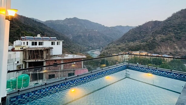 Una piscina infinita con vistas a la montaña, un edificio con paneles solares y un cielo despejado.