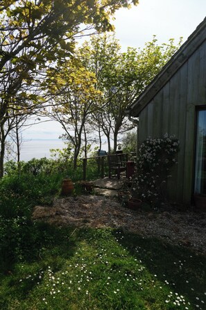 Ein rustikales Holzhaus mit Garten, einer Holzbank und Blick auf das Wasser.