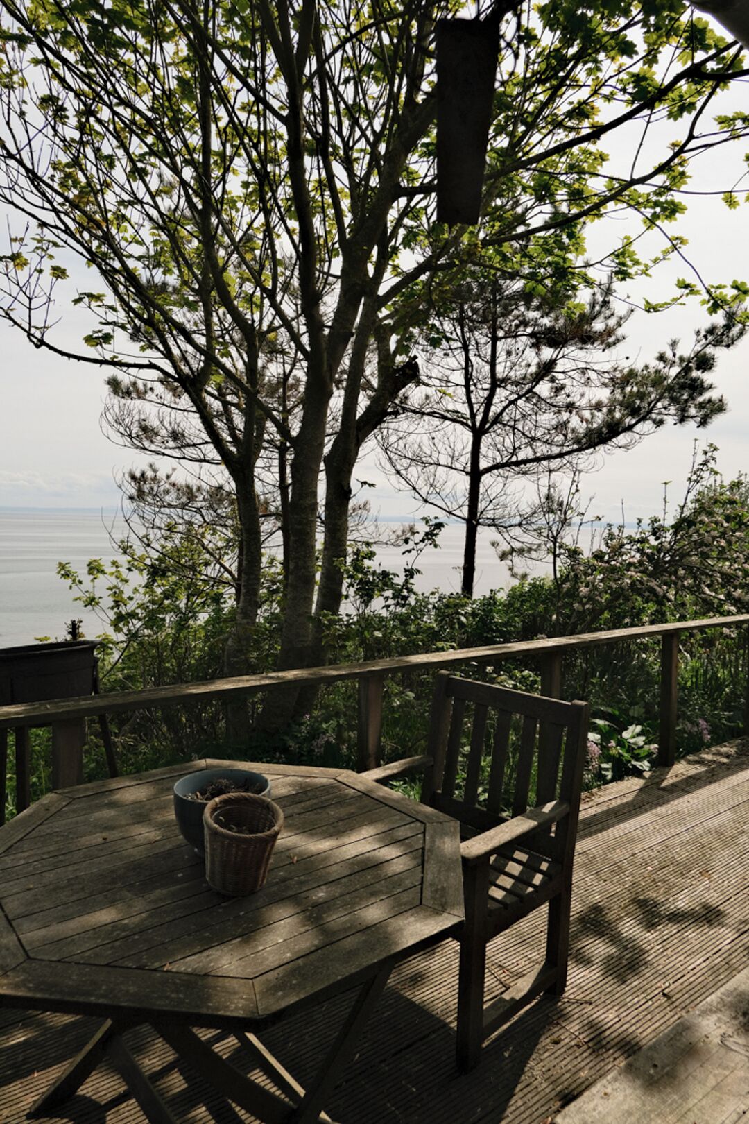 Um deck de madeira com uma mesa redonda e uma cadeira, com vista para a água.