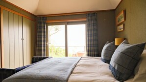 Een slaapkamer met een bed, gordijnen, een raam en een wandlamp.