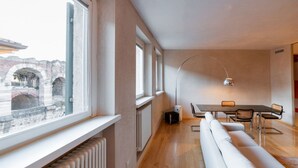 A modern interior with a dining area, a sofa, and a view of an outdoor brick structure. - Stunning residence with unique view of the Arena (Verona)