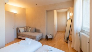 Hotellihuone, jossa on kaksi sänkyä, sohva, pieni pöytä, peili ja patteri.