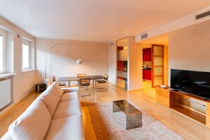 Un saló modern amb un sofà, taula de dinar, cadires, un televisor i una zona de cuina.
