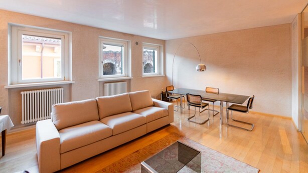 A modern living room with a sofa, dining table, chairs, and large windows. - Stunning residence with unique view of the Arena (Verona)