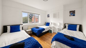 A modern bedroom with two beds, a window, and a small desk.