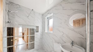 A modern bathroom with a shower, toilet, and sink, marble walls, and a mirror.