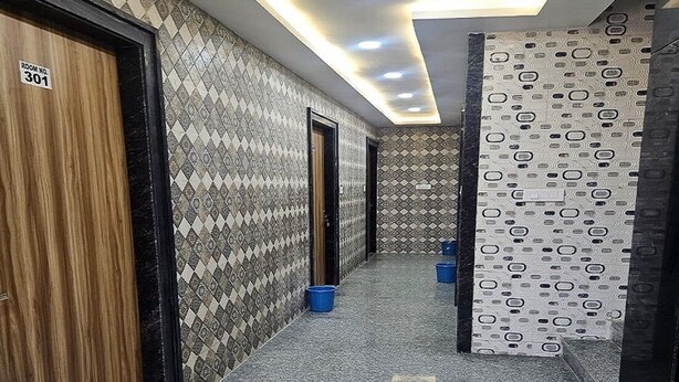 Un pasillo con paredes estampadas, una puerta de madera con la leyenda 'ROOM NO. 301' y cubos azules en el suelo.