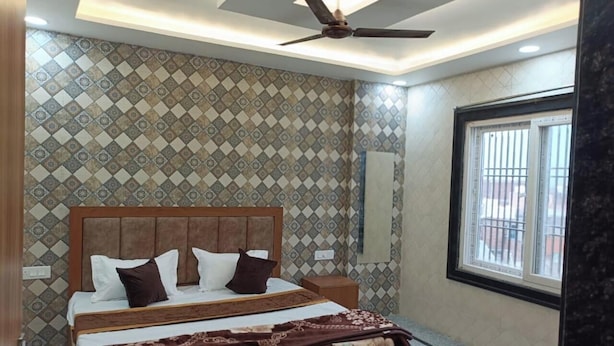 Une chambre avec un mur à motifs, un ventilateur de plafond, un lit avec des oreillers et une fenêtre avec des barreaux.