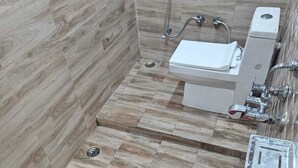 Une salle de bain avec une douche, des toilettes et un seau rouge posé sur une balance.