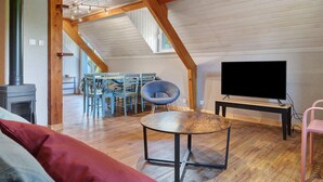 Et loft-studie med træloft, fjernsyn, et rundt bord og en pejs.
