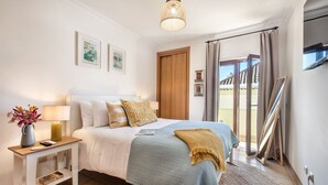 A bedroom with a bed, bedside table, lamp, and a view of the outside.
