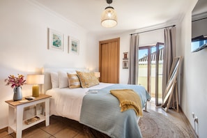 Ein Schlafzimmer mit Bett, Nachttisch, Lampe und Blick ins Freie.