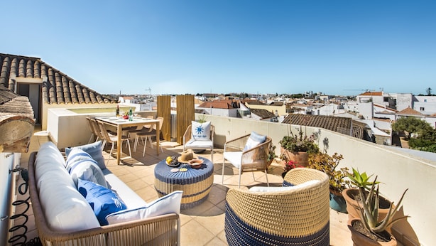A rooftop terrace with wicker furniture, a dining area, and potted plants.