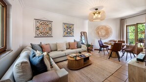 A living room with a sofa, coffee table, dining table, chairs, and artwork on the walls.