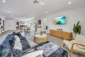 Ein modernes Wohnzimmer mit Sofa, Couchtisch und Fernseher. Im Hintergrund ist eine Küche zu sehen.