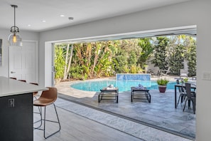 Eine moderne Küche mit Bar, ein Sitzbereich am Pool mit Liegestühlen und Blick auf einen üppigen Garten.