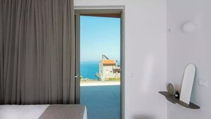 A bedroom with a bed, a bathroom with a toilet, and a view of the sea through an open door. - Plethora Luxury Suites (Malevizi)