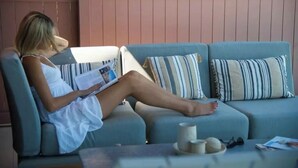 A person sitting on a sofa with striped pillows, reading a magazine. - Plethora Luxury Suites (Malevizi)