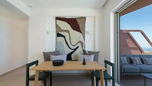 A modern interior with a dining area, a large abstract painting, and a view of a balcony with outdoor seating. - Plethora Luxury Suites (Malevizi)