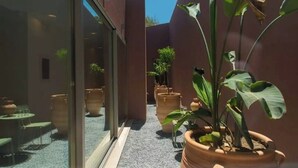 A narrow corridor with potted plants, a glass door, and a seating area with tables and chairs. - Plethora Luxury Suites (Malevizi)