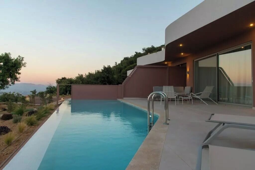 A modern pool area with a clear view of the landscape, a seating area with chairs, and a glass door entrance.