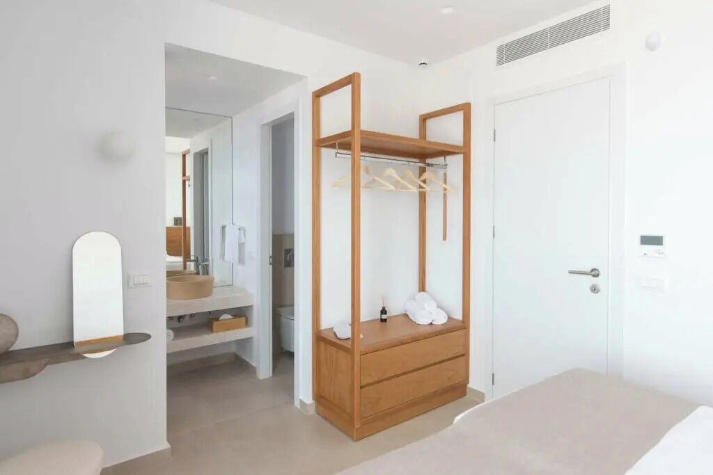 Un dormitorio con un armario de madera, una mesita de noche, un espejo y una puerta.
