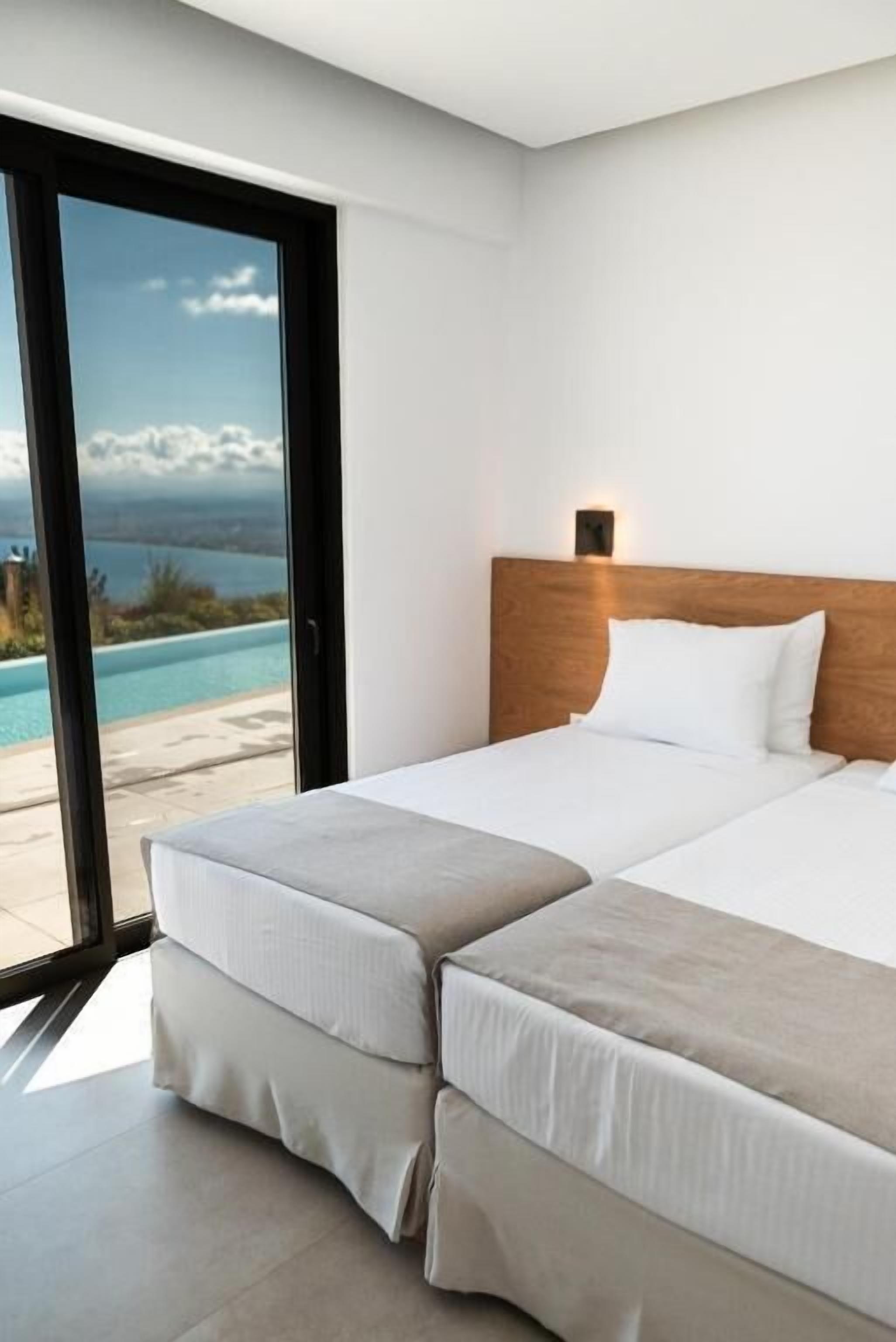Habitación de hotel con un amplio ventanal corredero que da a una piscina, cabecera de madera y cama con ropa blanca.