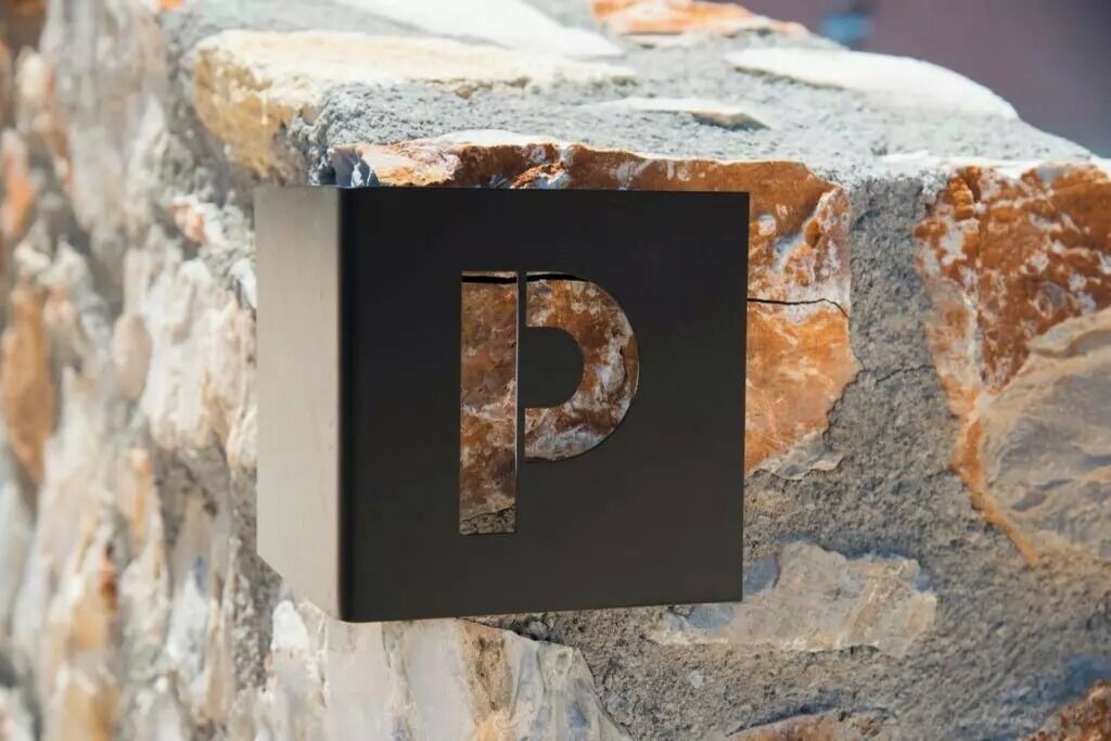 A black sign with a large, metallic 'P' on a stone wall.
