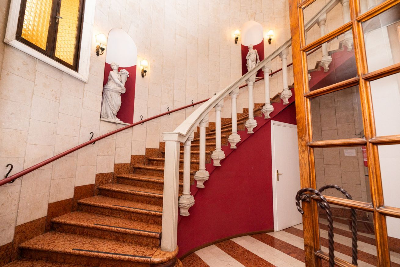 A staircase with white balusters, a red wall, and a statue.