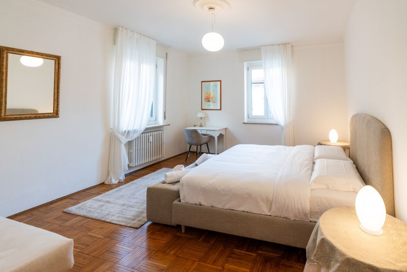 A bedroom with a bed, a desk, a chair, a radiator, and a window with curtains.