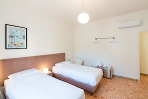 Ein Hotelzimmer mit zwei Betten, einem Bild an der Wand, einer Pendelleuchte und einer Klimaanlage.