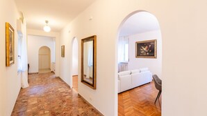 Un couloir avec un parquet en chevrons, des murs blancs et un canapé blanc dans une pièce.