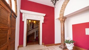 Un couloir aux murs rouges, avec une porte blanche, un escalier et une colonne.