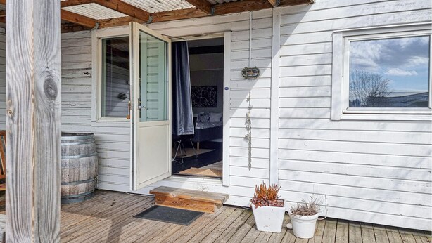 A wooden cabin with a porch, a door leading to a bedroom, and a window with a view.