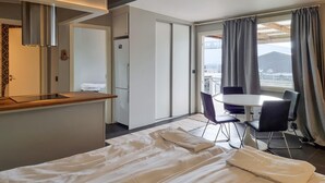 A hotel room with a bed, a small desk, a chair, a table, and a view of the outside.