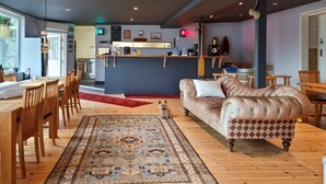 A cozy living area with a sofa, dining table, chairs, a rug, and a kitchen in the background.