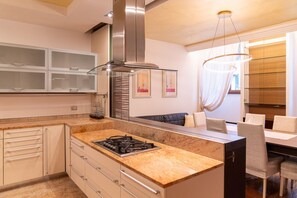 A modern kitchen with a gas stove, stainless steel range hood, and a dining area with a table and chairs. - Luxurious residence with large terrace overlooking Arena (Verona)