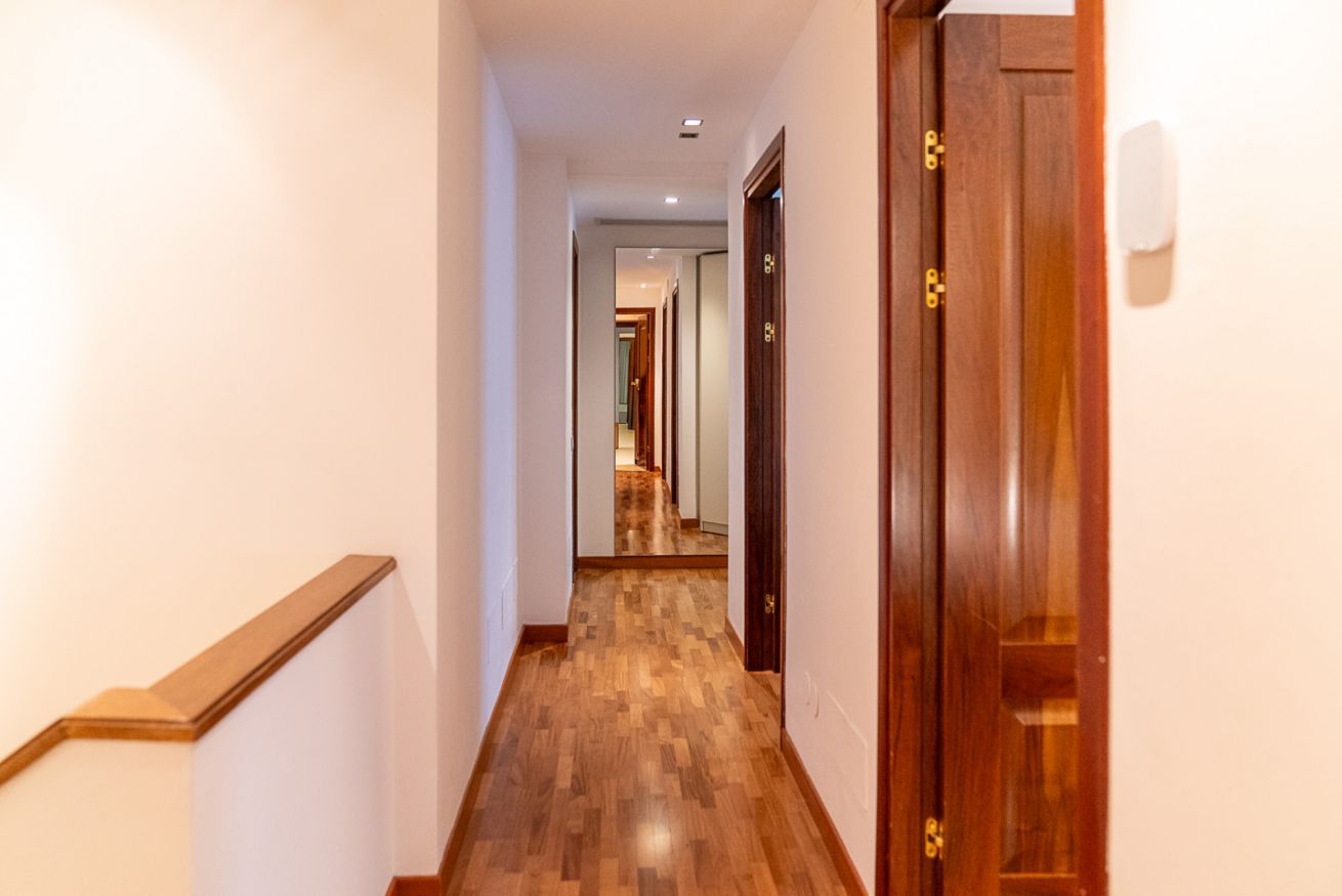 Un pasillo con suelo de madera, una puerta de madera a la derecha y una escalera a la izquierda.